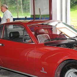Un homme se tient à côté d'une voiture rouge avec le capot ouvert.