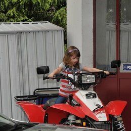 Une petite fille conduit un VTT rouge et blanc à côté d'une voiture.