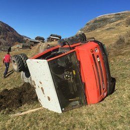 Un tracteur rouge est retourné sur le côté dans un champ.