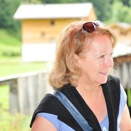 Une femme portant des lunettes de soleil et une chemise bleue sourit.