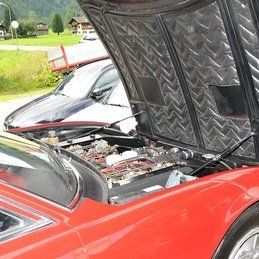 Une voiture rouge avec le capot ouvert est garée à côté d'une voiture noire.