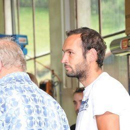 Un homme barbu se tient à côté d'un autre homme dans une pièce.