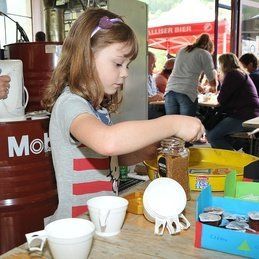 Une petite fille est assise à une table et joue avec des tasses et des bocaux.