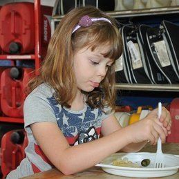 Une petite fille est assise à une table avec une assiette de nourriture et une fourchette.