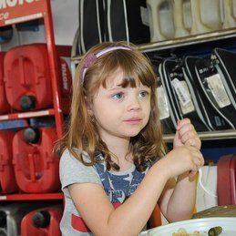 Une petite fille est assise à une table avec une assiette de nourriture.