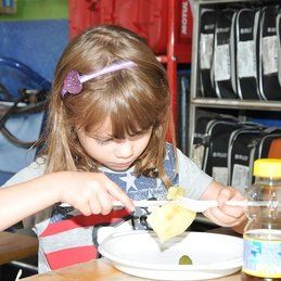 Une petite fille est assise à une table en train de manger de la nourriture dans une assiette.