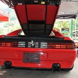 Une Ferrari rouge avec le capot relevé est garée devant une tente.