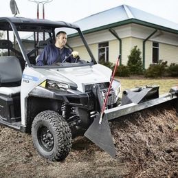 Un homme conduit un véhicule utilitaire Polaris auquel est attachée une charrue.