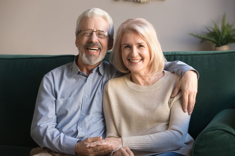 A smiling couple sits closely together on a green couch, holding hands in a bright, modern living space.