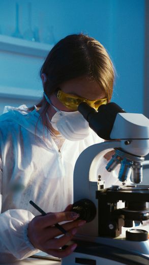 Scientist in protective gear looking through a microscope in a lab.