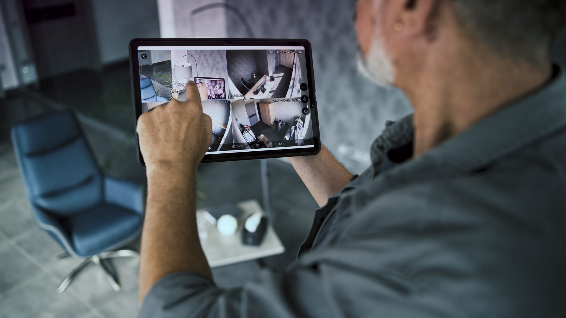 Man using a tablet to view security camera feeds inside a home office.