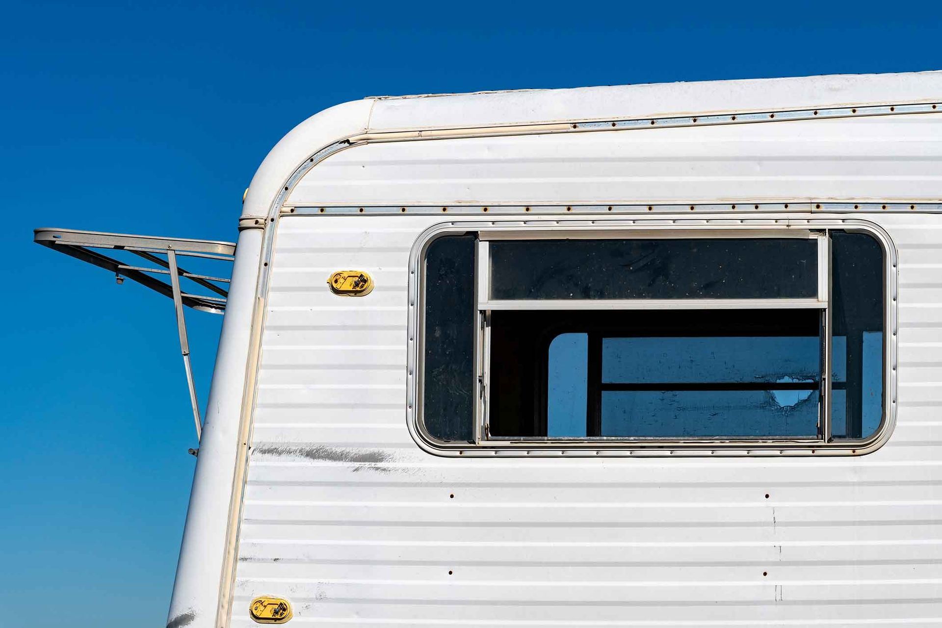 White camper with a partially open window against a clear blue sky.