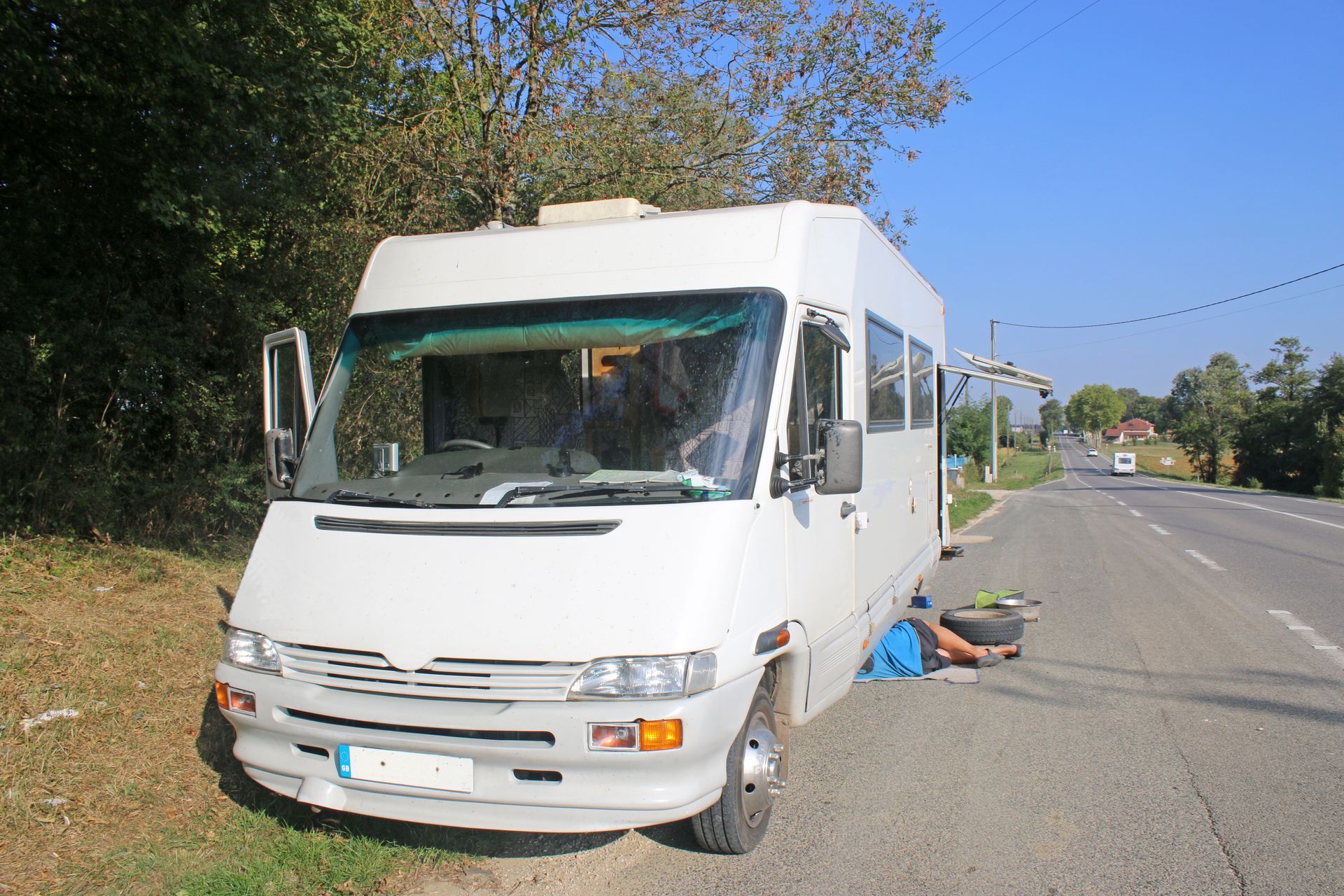 White camper van parked on roadside, person working on the wheel.
