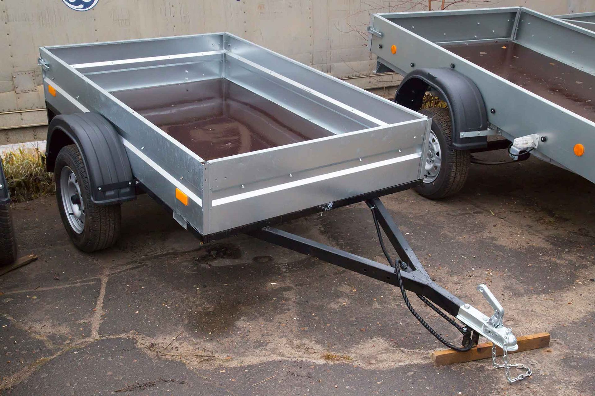 A small, silver utility trailer with black tires and a hitch parked on pavement.