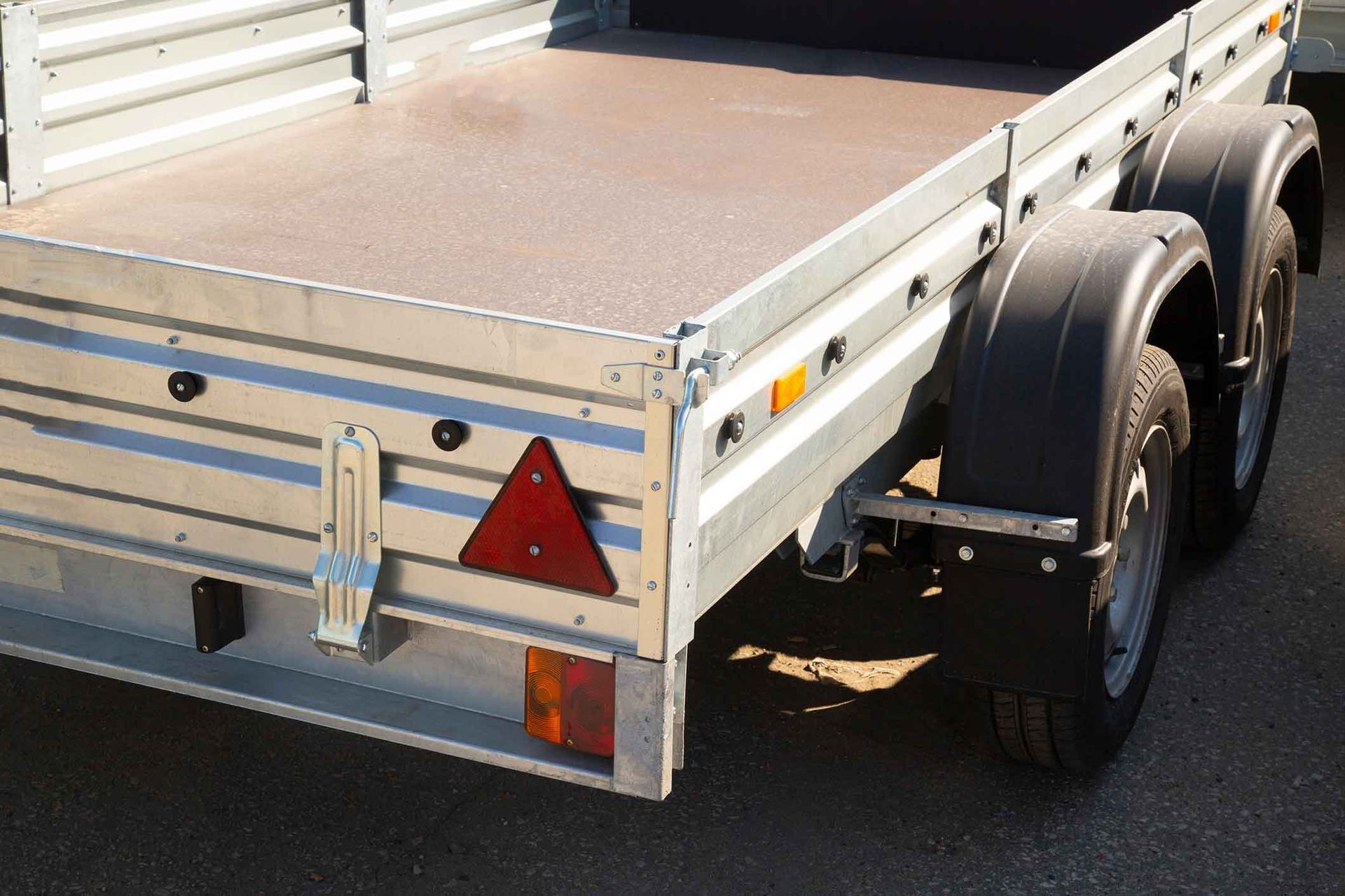 Silver utility trailer with two tires, brown bed, and a red triangle safety marker.