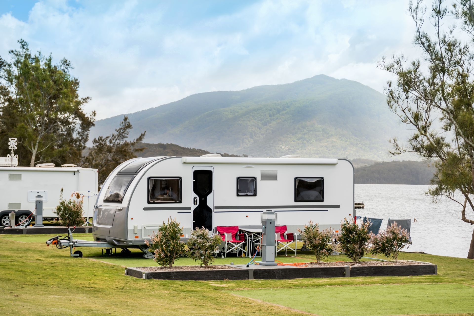 Caravan parked on grassy campsite near a body of water with mountains in the background.