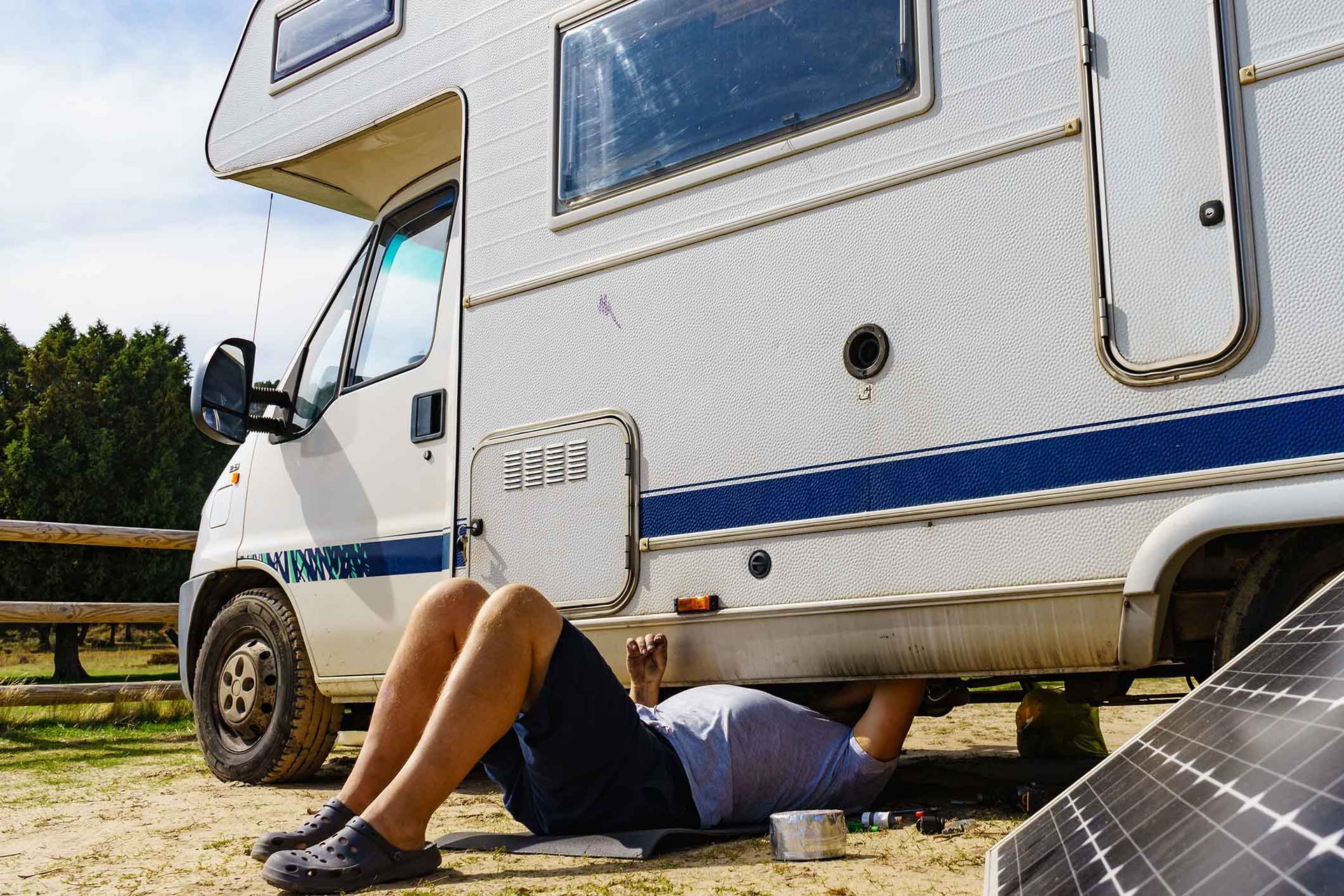 Person working on the underside of a white RV. Solar panel is in the foreground.