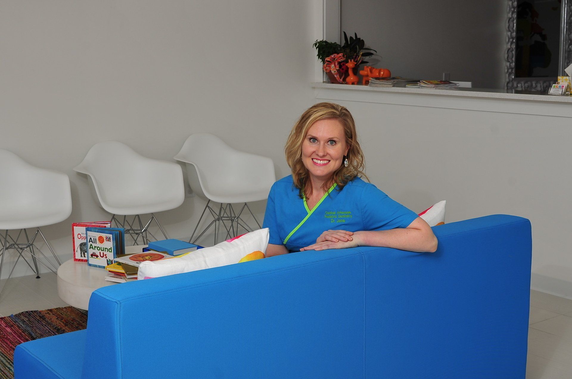 A woman is sitting on a blue couch in a waiting room.