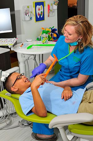 A young boy is laying in a dental chair while a female dentist examines his teeth.