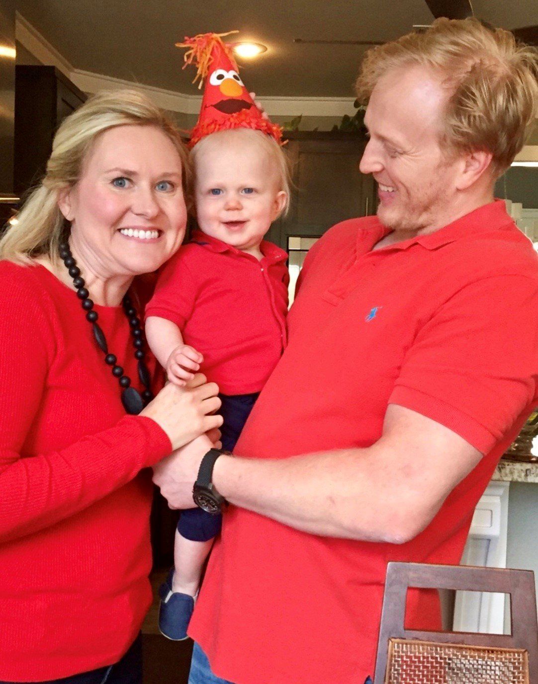 A man and woman holding a baby wearing elmo hats