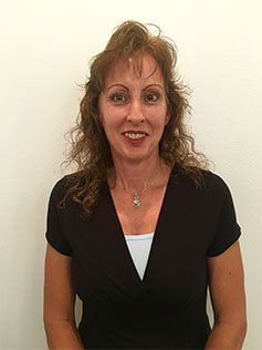 A woman wearing a black shirt and a necklace is smiling for the camera.