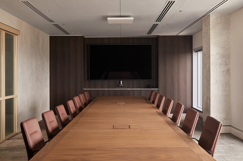 Modern conference room with a long wooden table, brown chairs, and a large wall-mounted screen