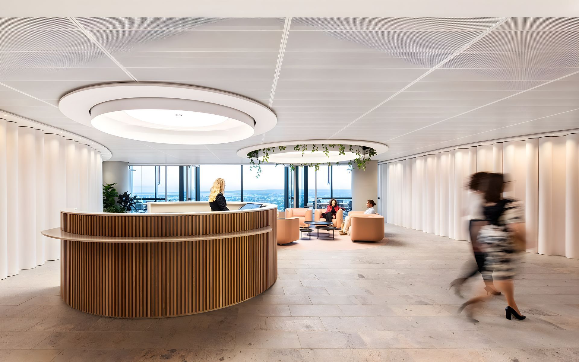 Modern office lobby with a curved wooden reception desk and blurred person walking past large windows