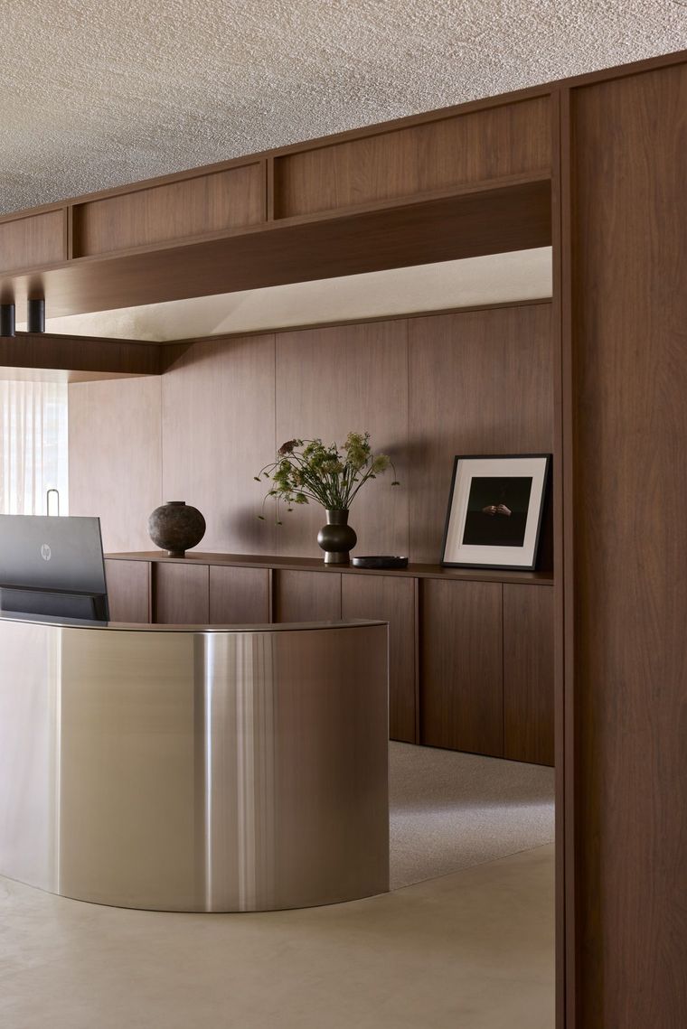 Modern reception desk with wood paneling, metallic counter, and decorative vase and framed photo in a lobby