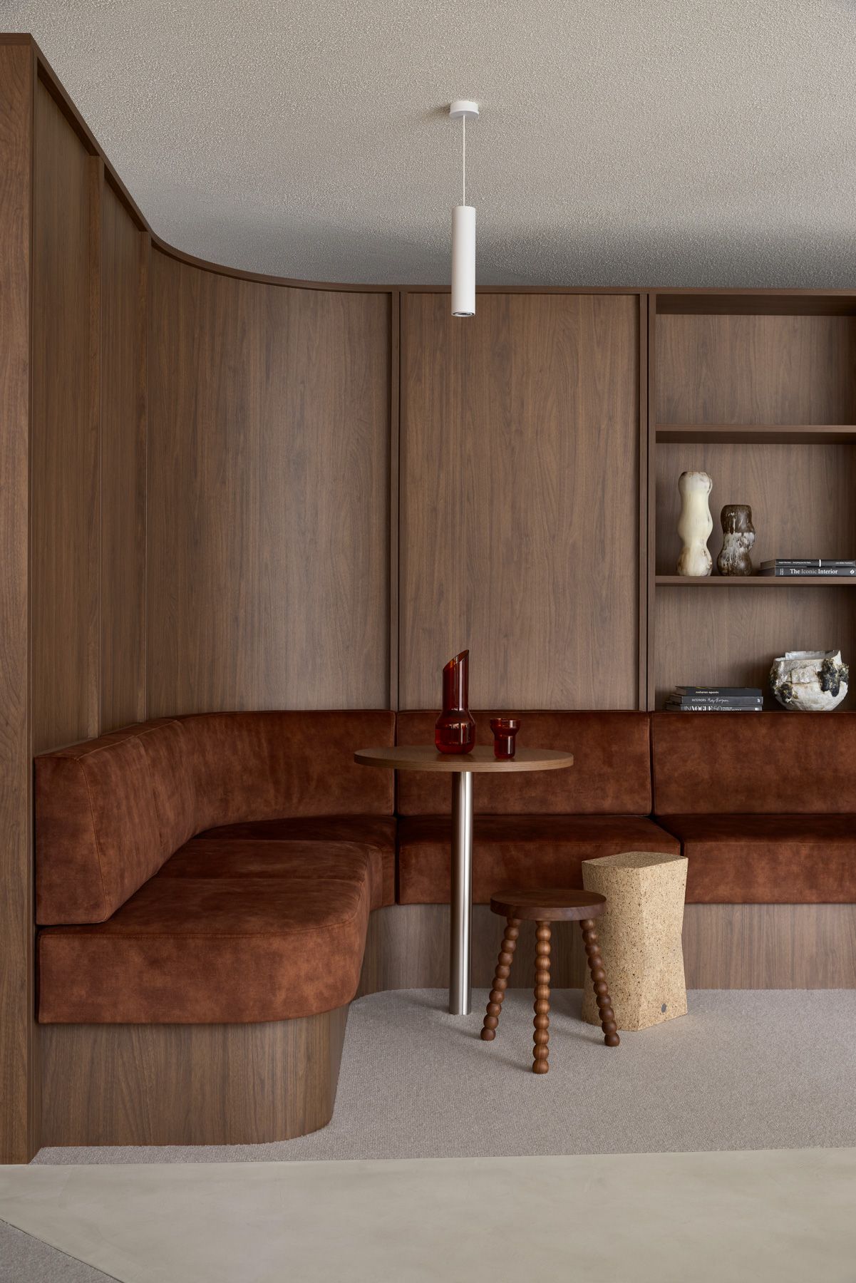 Curved brown built-in bench in a cozy wood-paneled room with a small table, stool, and shelves