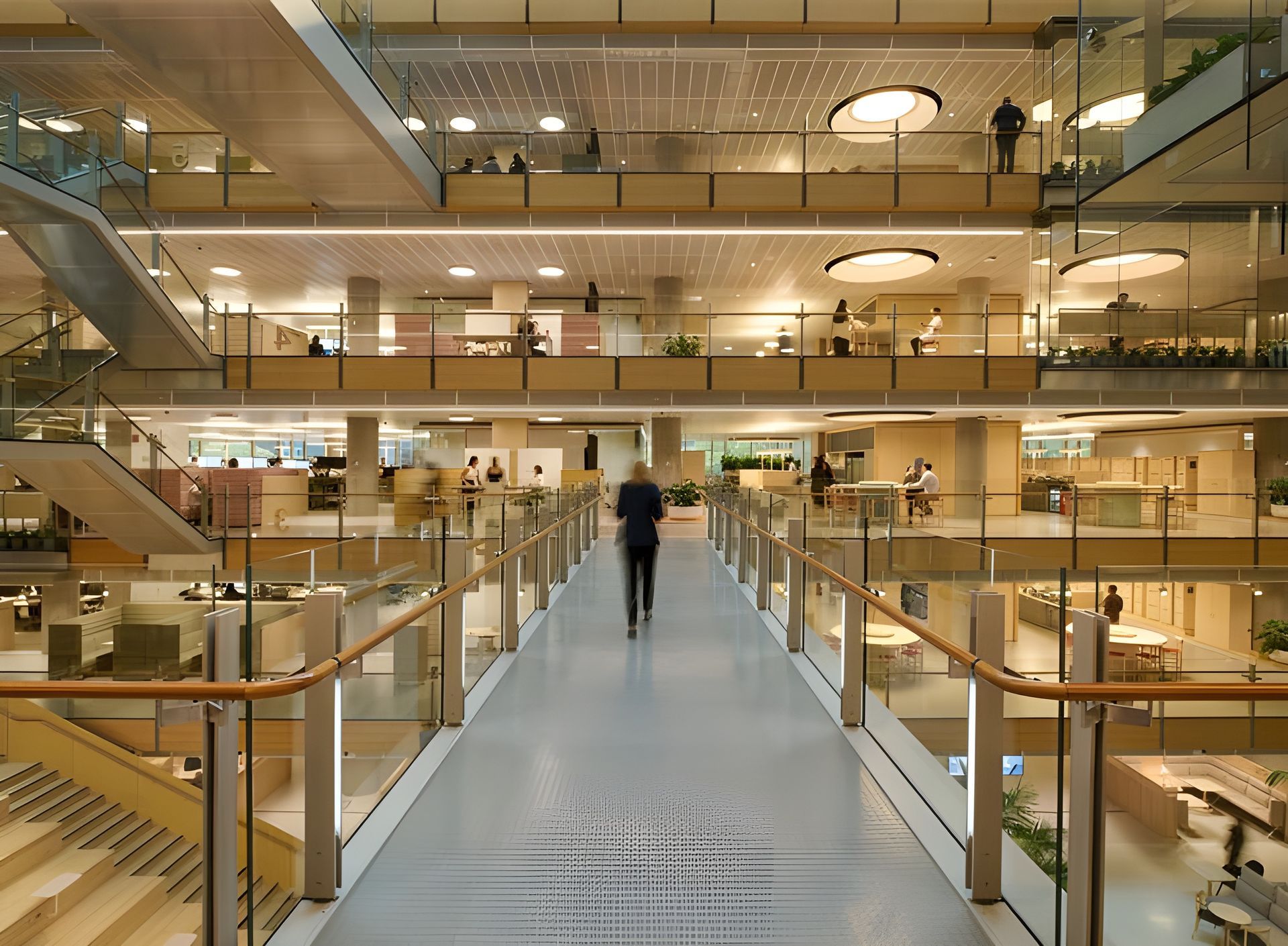 Modern indoor atrium with glass railings and a lone person walking on a central blue walkway