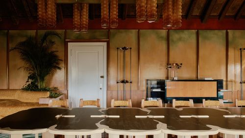 Empty restaurant interior with wooden tables, white chairs, and a counter under warm lighting