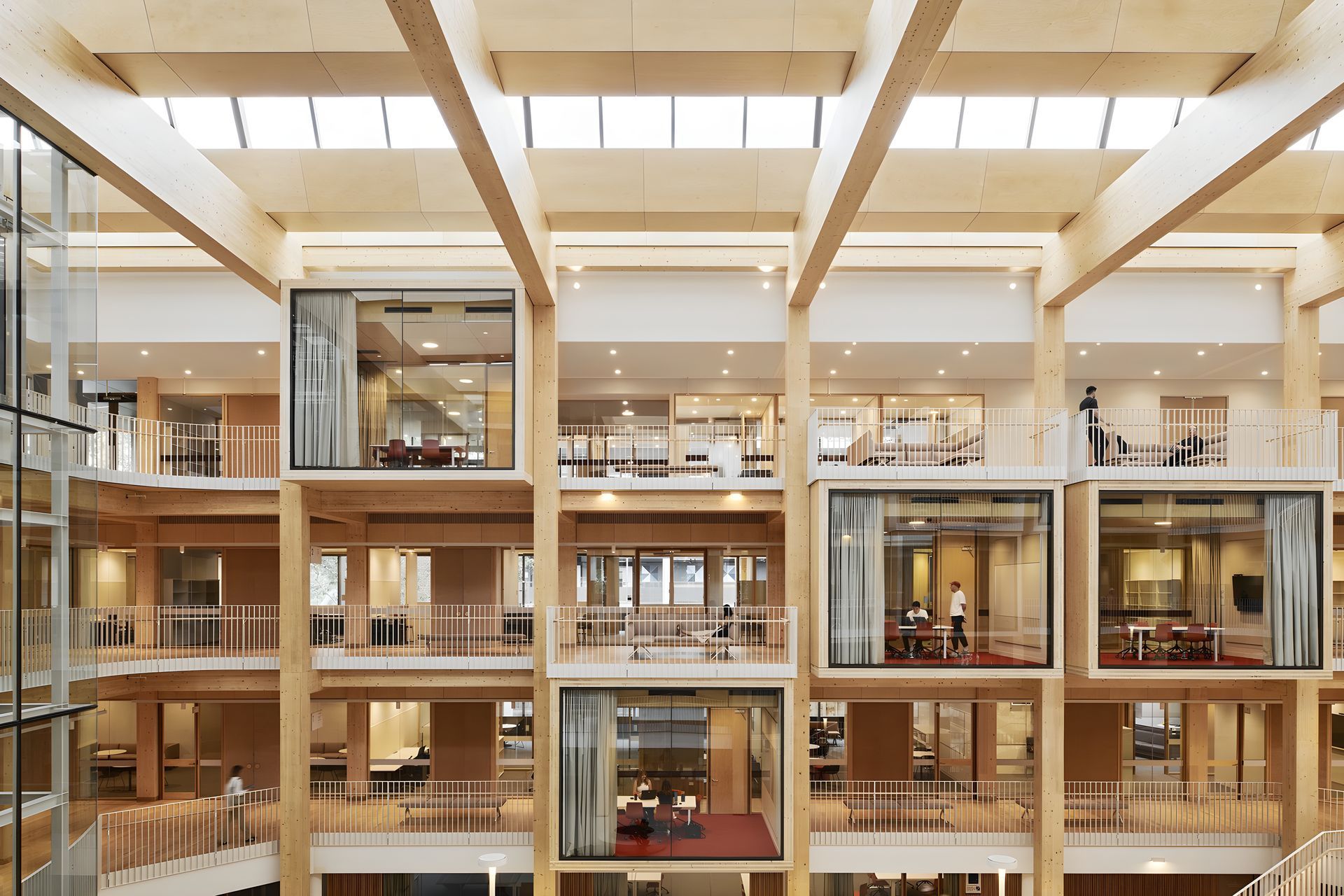 Interior of a modern office atrium with glass-walled rooms, wooden beams, and warm lighting