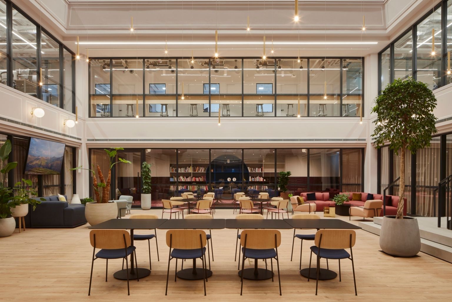 Modern hotel lobby with warm seating, a long table, and large glass walls under soft lighting
