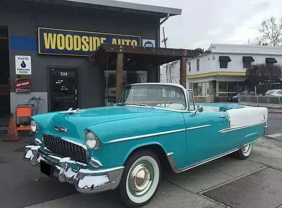 Turquoise 1955 Chevrolet Bel Air convertible parked in front of Woodside Auto shop.