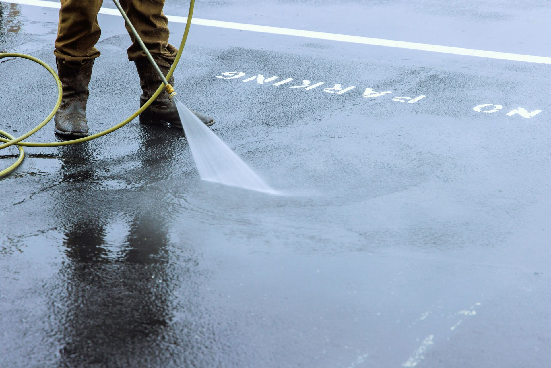 A person is using a high pressure washer to clean a parking lot