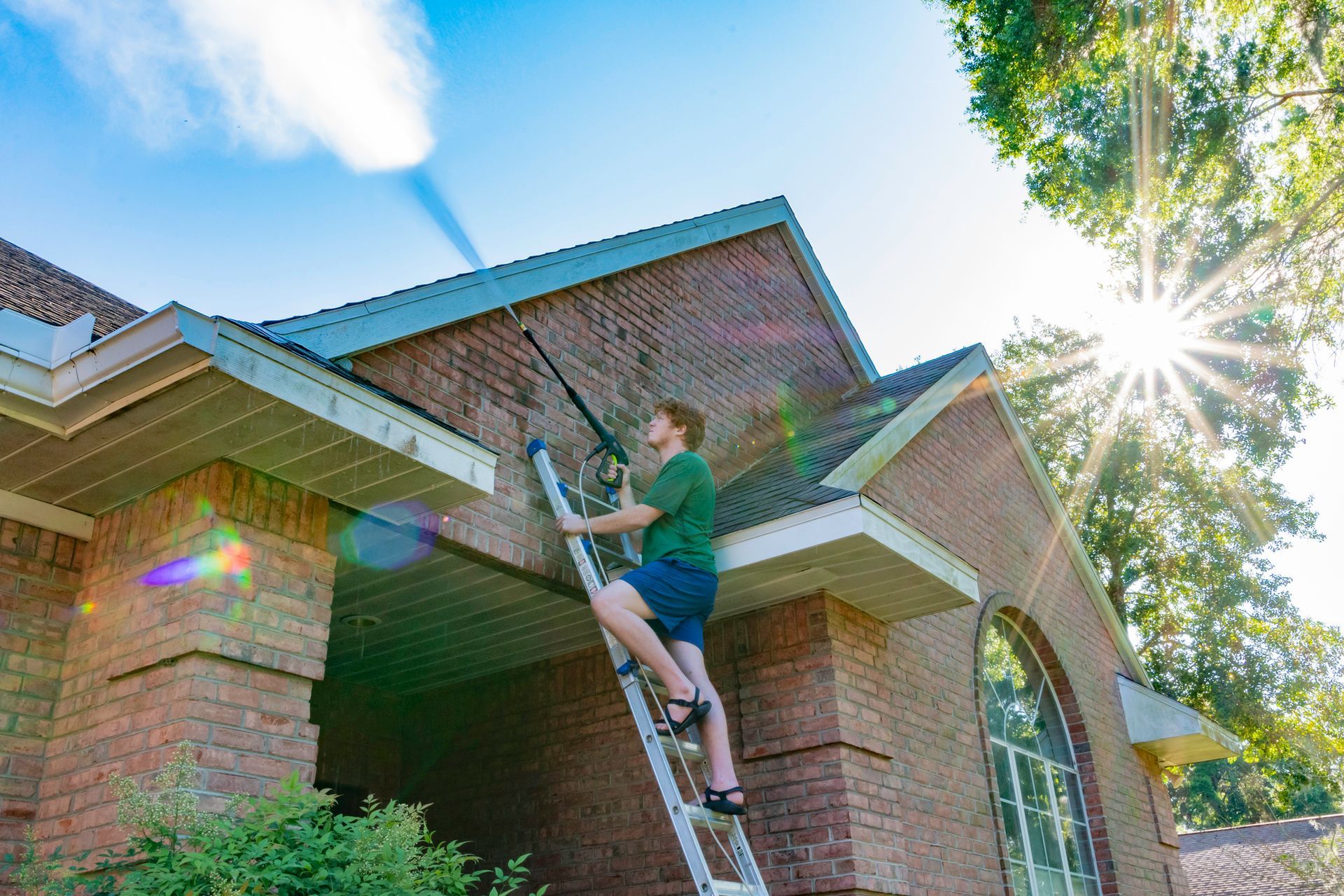 A man is cleaning the roof of a brick house with a pressure washer.
