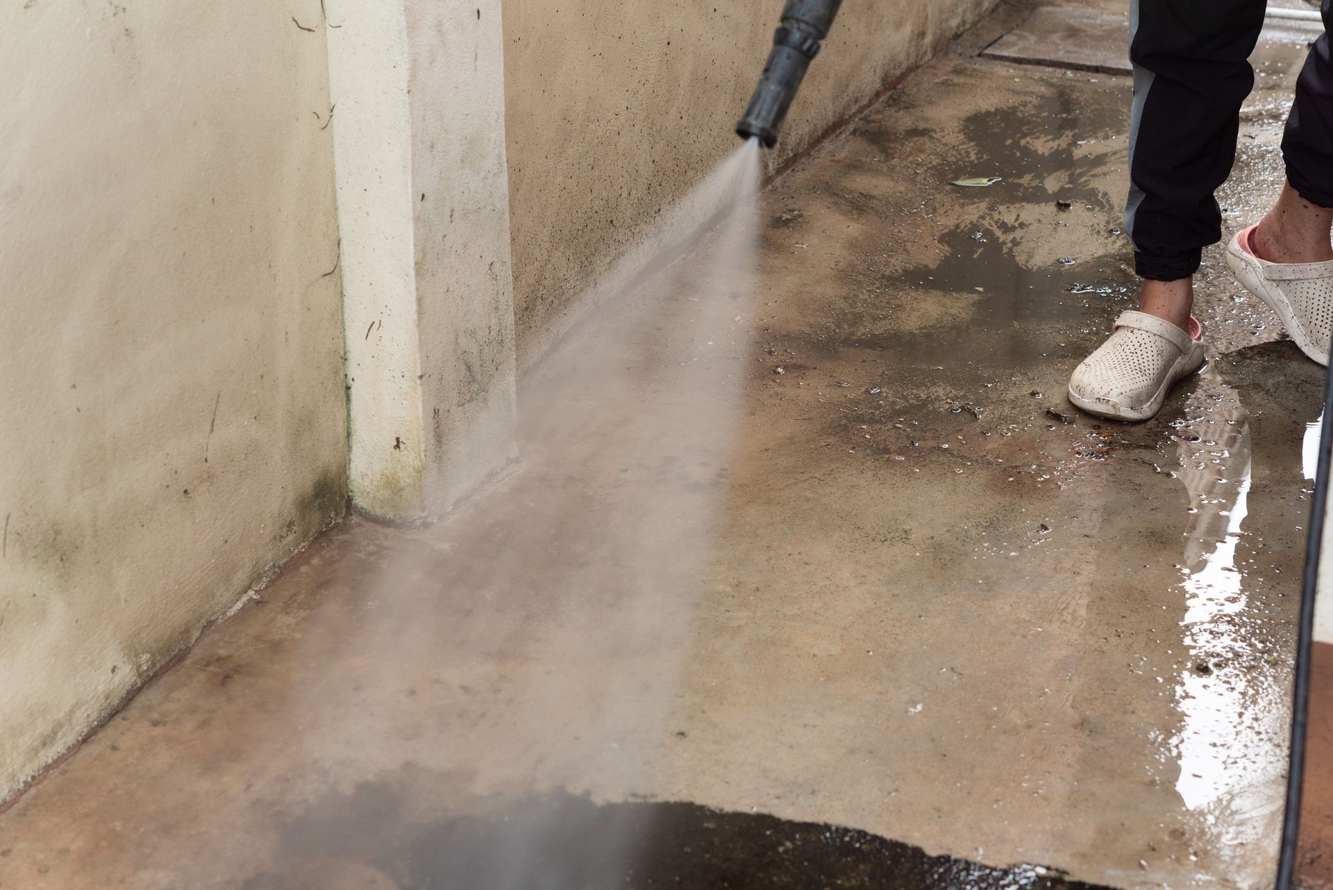 A person is using a high pressure washer to clean a concrete floor.