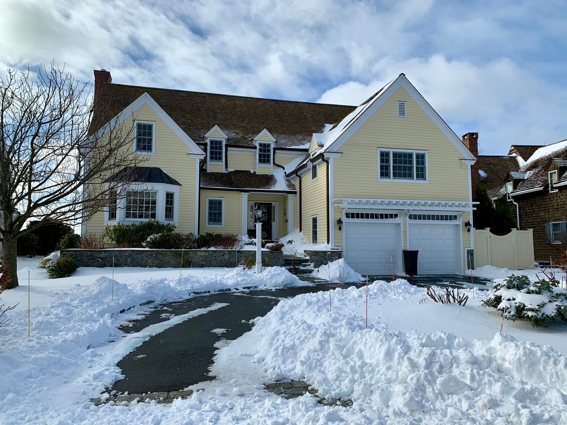 A large yellow house is surrounded by fresh snow. It is a double story home with large windows & a double garage. The snow has been cleared.