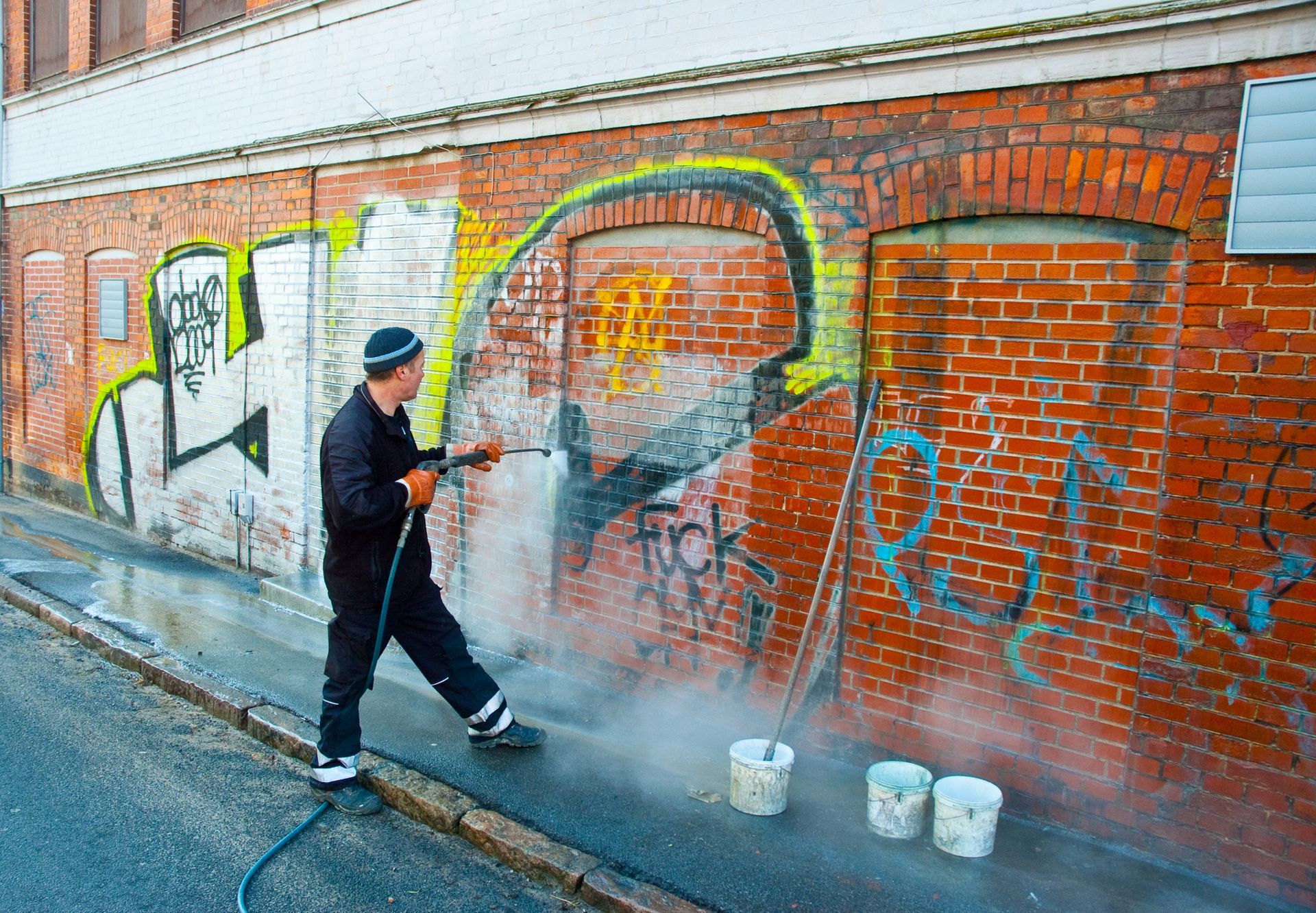 A man is cleaning graffiti on a brick wall with a high pressure washer.