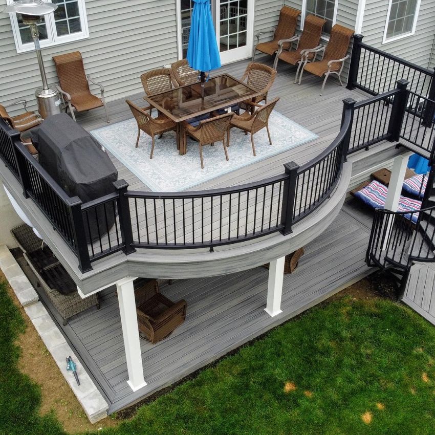 Back deck patio with black railing, outdoor dining set, blue umbrella, and grill above a lower patio