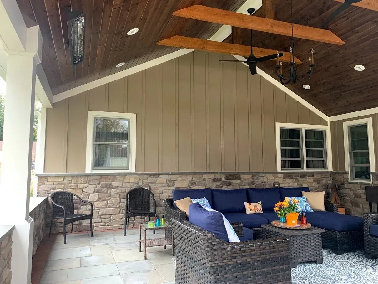Patio with brown siding, stone wall, blue couch, and wooden ceiling.