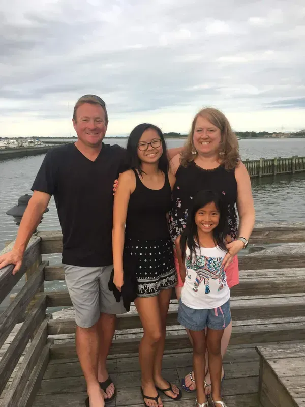 Family of four posing together on a wooden pier. Cloudy sky.
