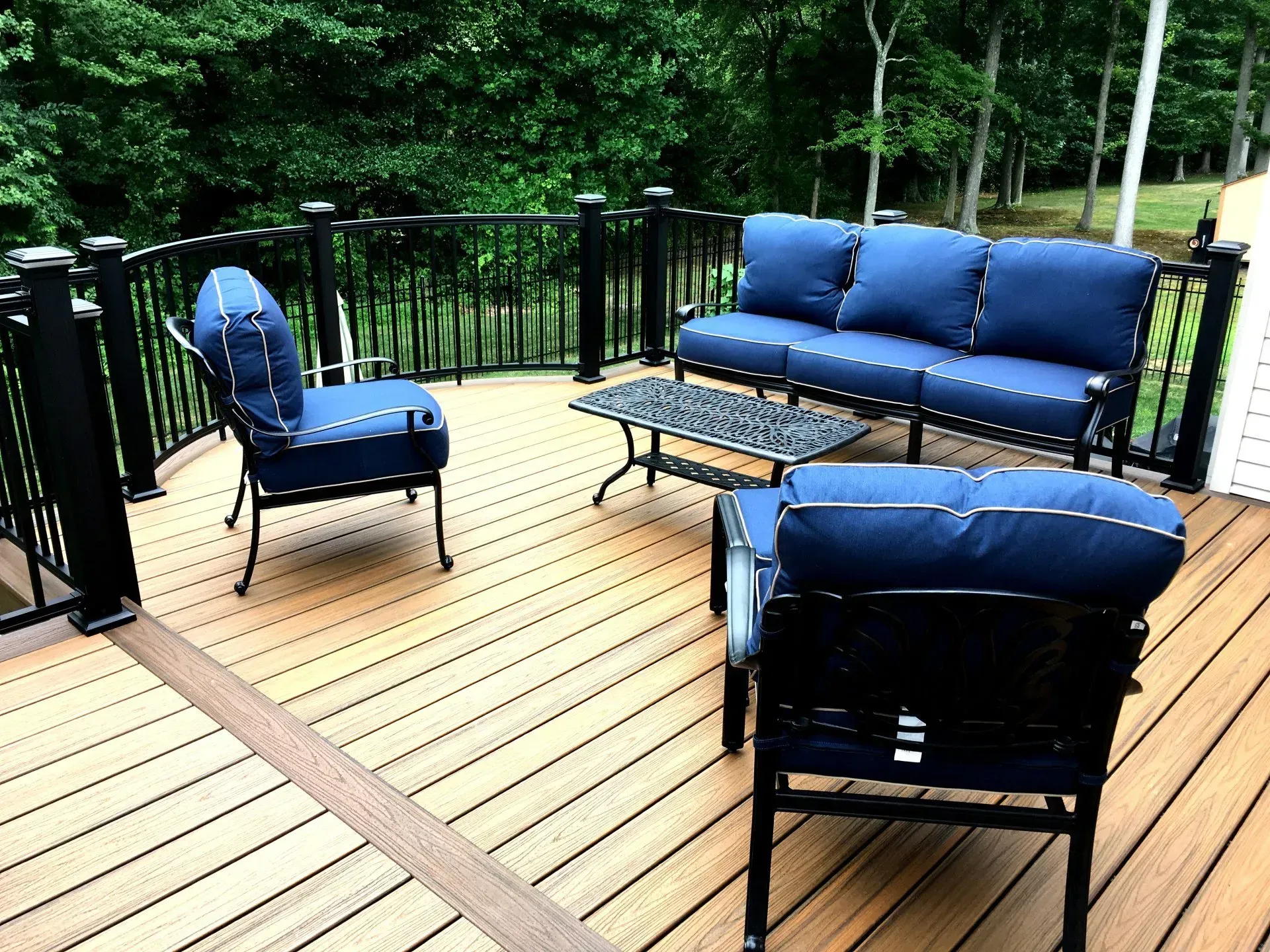Outdoor deck with blue cushioned seating, black railings, and a small metal table.