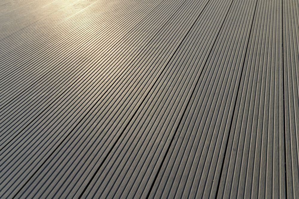 Aerial view of a backyard with a hot tub, deck, seating, and umbrella, next to a house with a gray roof.