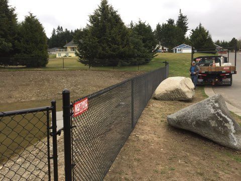 A Chain Link Fence Is Being Built Next to A Large Rock - Sequim, WA- NW Chainlink Fence Co