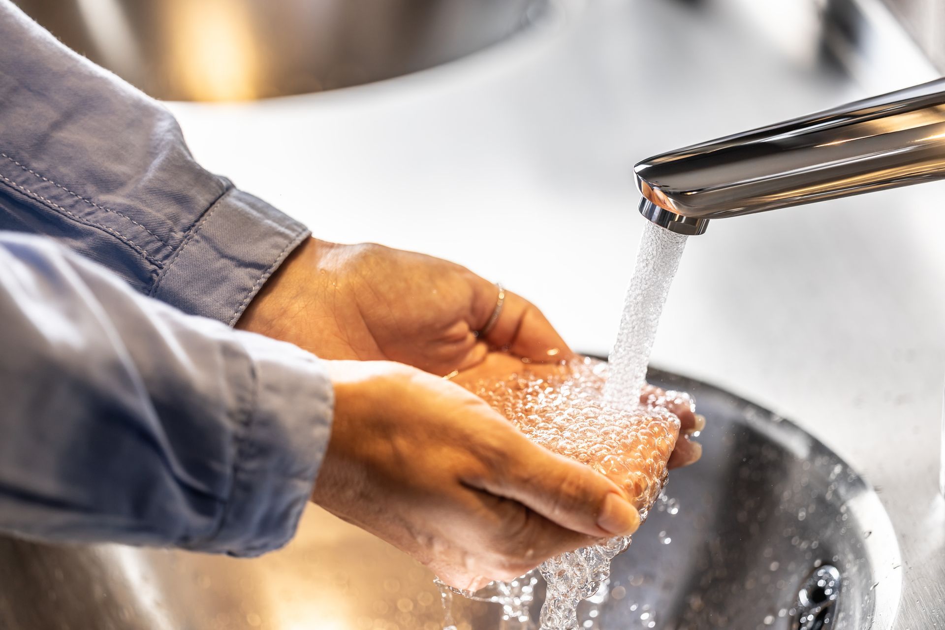 Man washing her hands under running water in a bathroom.