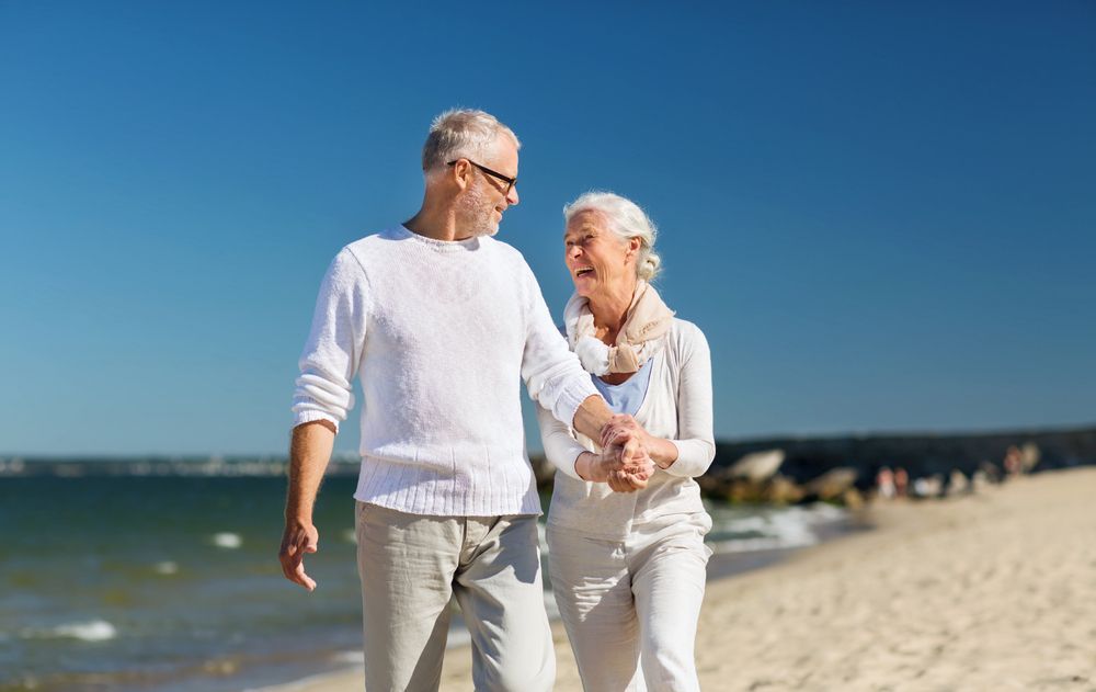 An Elderly Couple is Walking on the Beach Holding Hands — NH Legal In Wollongong, NSW