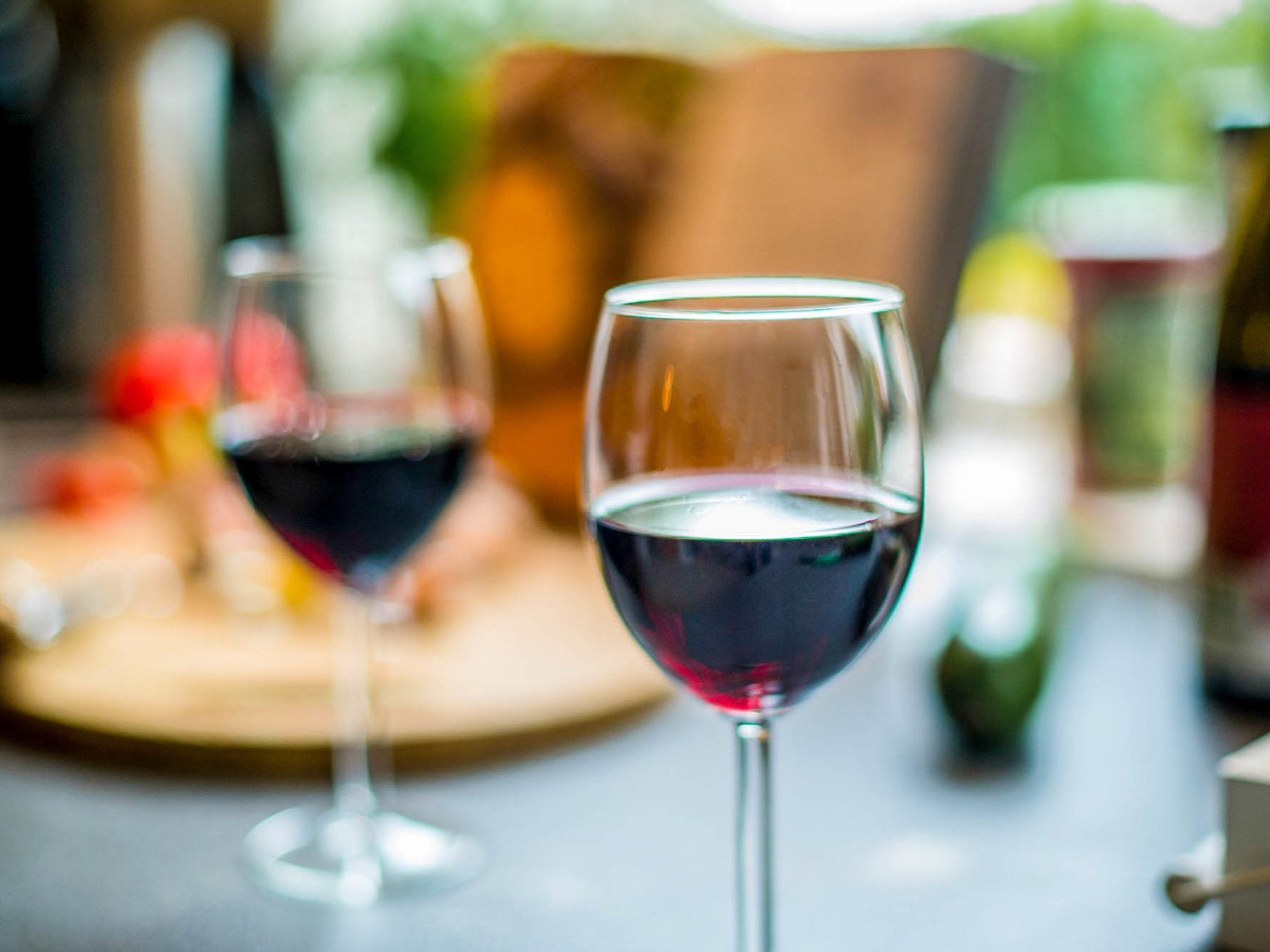 Zwei mit Rotwein gefüllte Weingläser, im Hintergrund verschwommenes Essen und eine Szenerie im Freien.