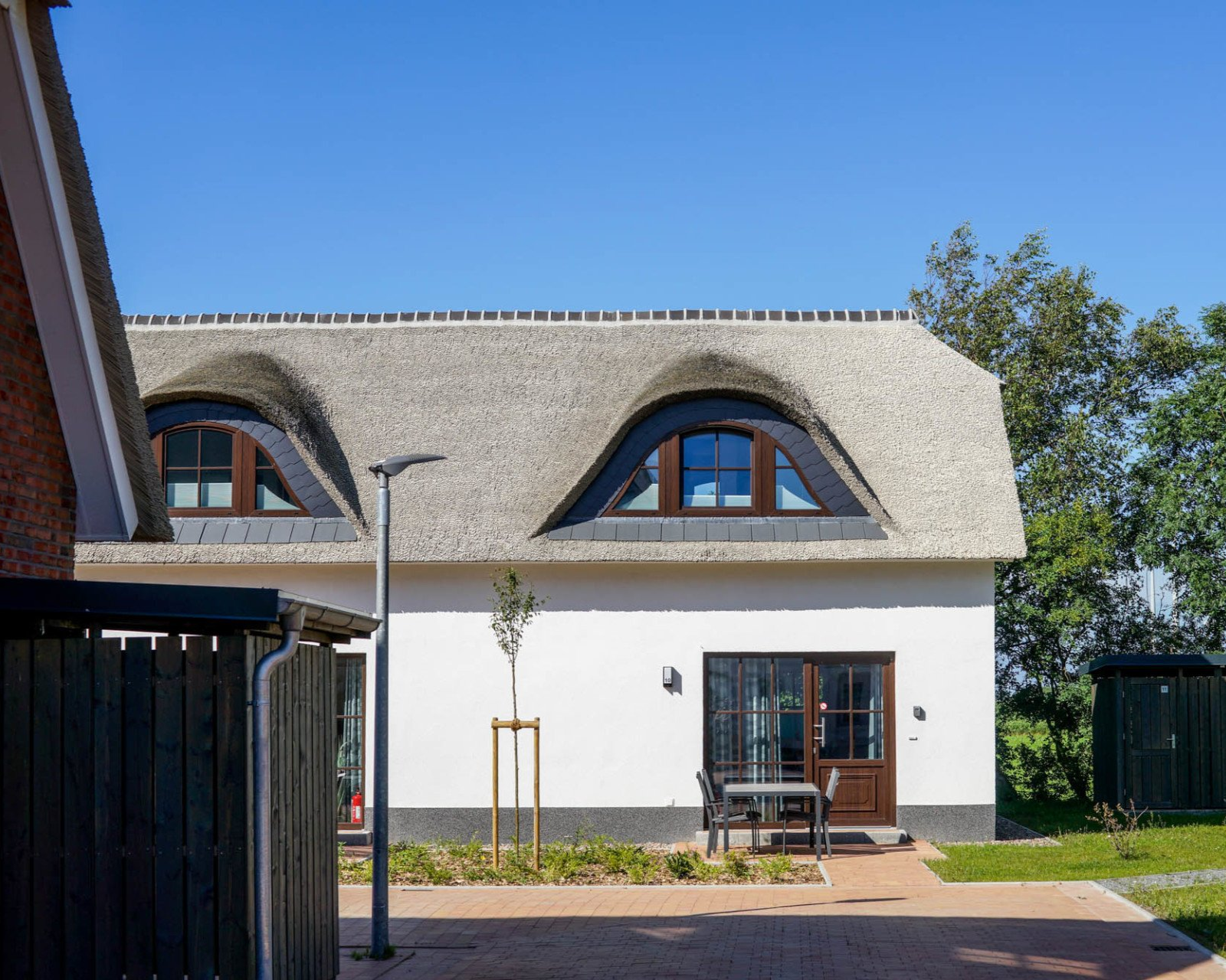 Weißes Häuschen mit Reetdach und Bogengaubenfenstern an einem sonnigen Tag.