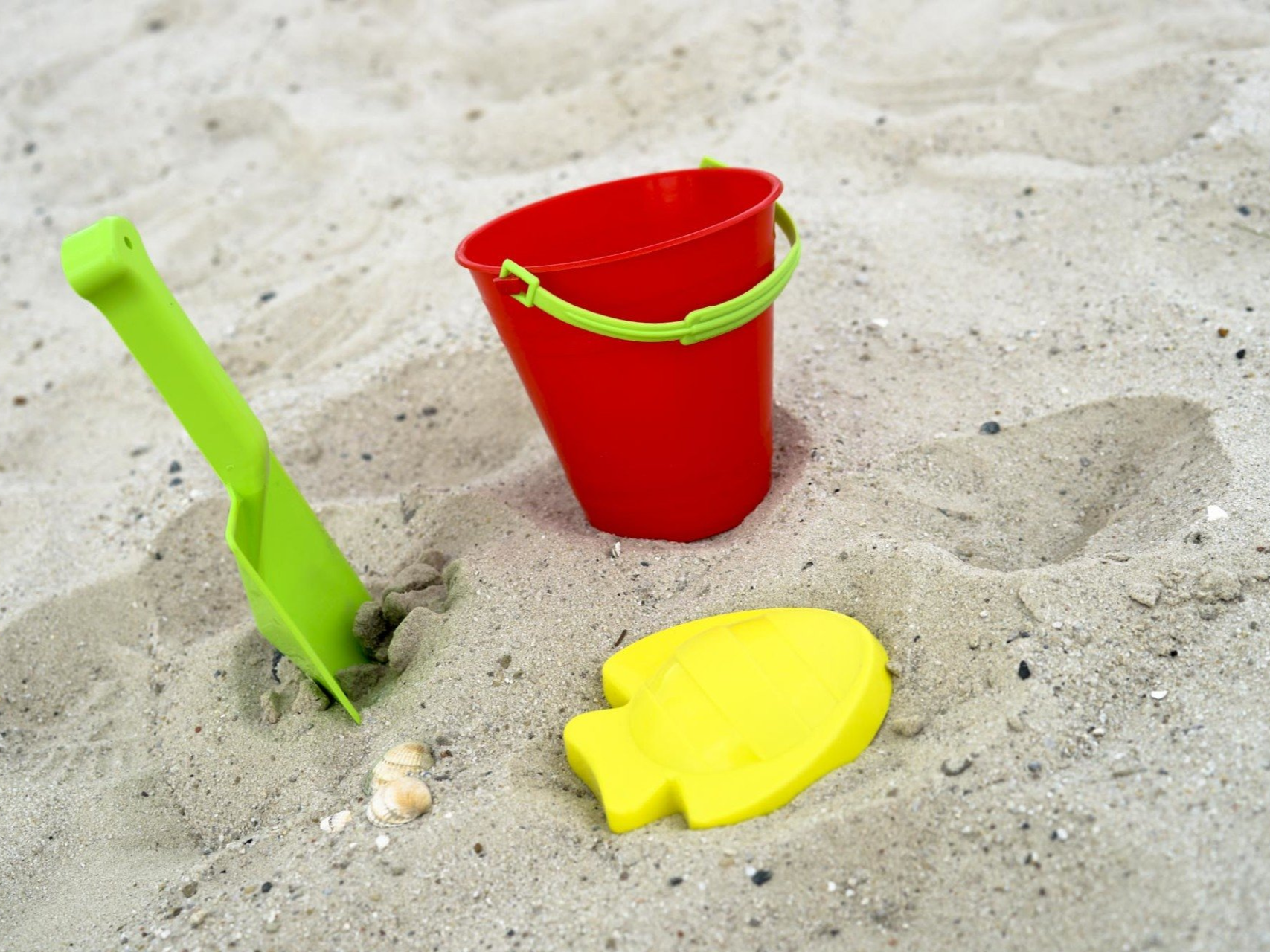 Roter Eimer, gelbe fischförmige Form und grüne Schaufel im Sand.